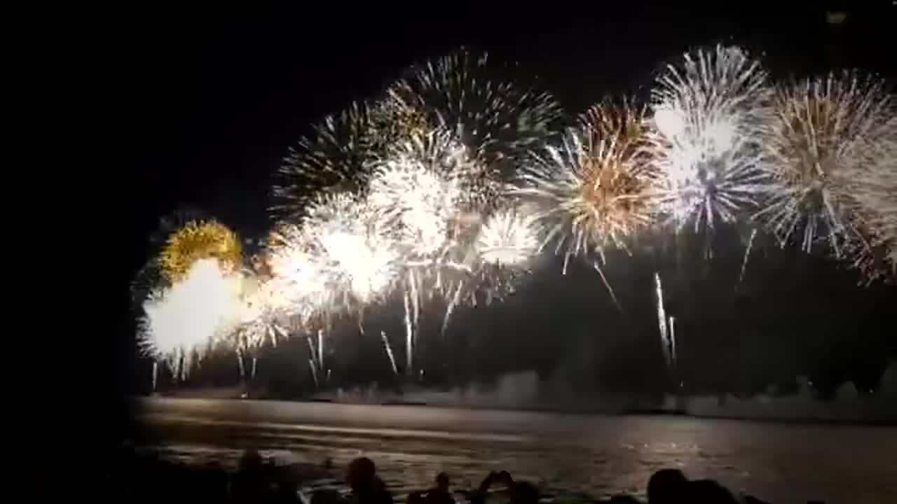 Fireworks over the water at Copacabana at night, with the crowd in silhouette along the shore.
